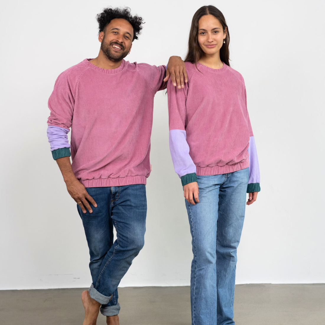  Eine Frau und ein Mann stehen beide lächelnd nebeneinander und tragen dabei den pinken Unisex Sweater von Oktopulli