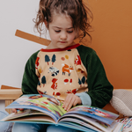 Ein Kind liest ein Buch und trägt dabei den genderneutralen Alltagsbegleiter von Oktopulli mit dem Motiv Waldgewusel