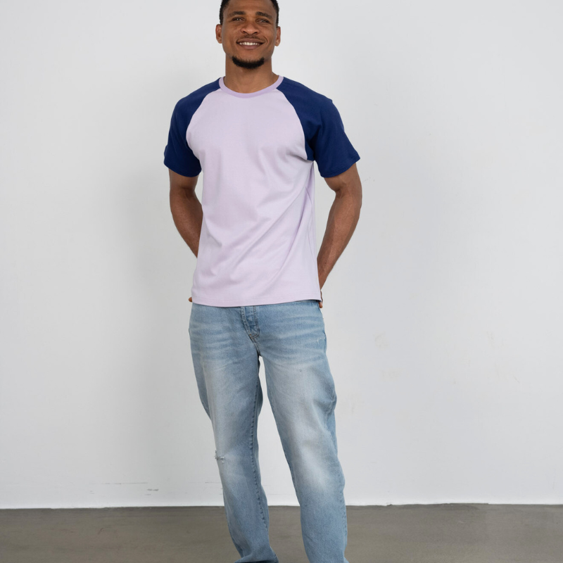 Ein Mann steht vor einer Wand und trägt ein Raglan Shirt aus Bio-Baumwolle von Oktopulli in den Farben Flieder und Blau