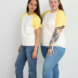  Zwei Frauen tragen ein weißes Raglan T-Shirt der Marke Oktopulli mit gelb-weiß gestreiften Ärmeln