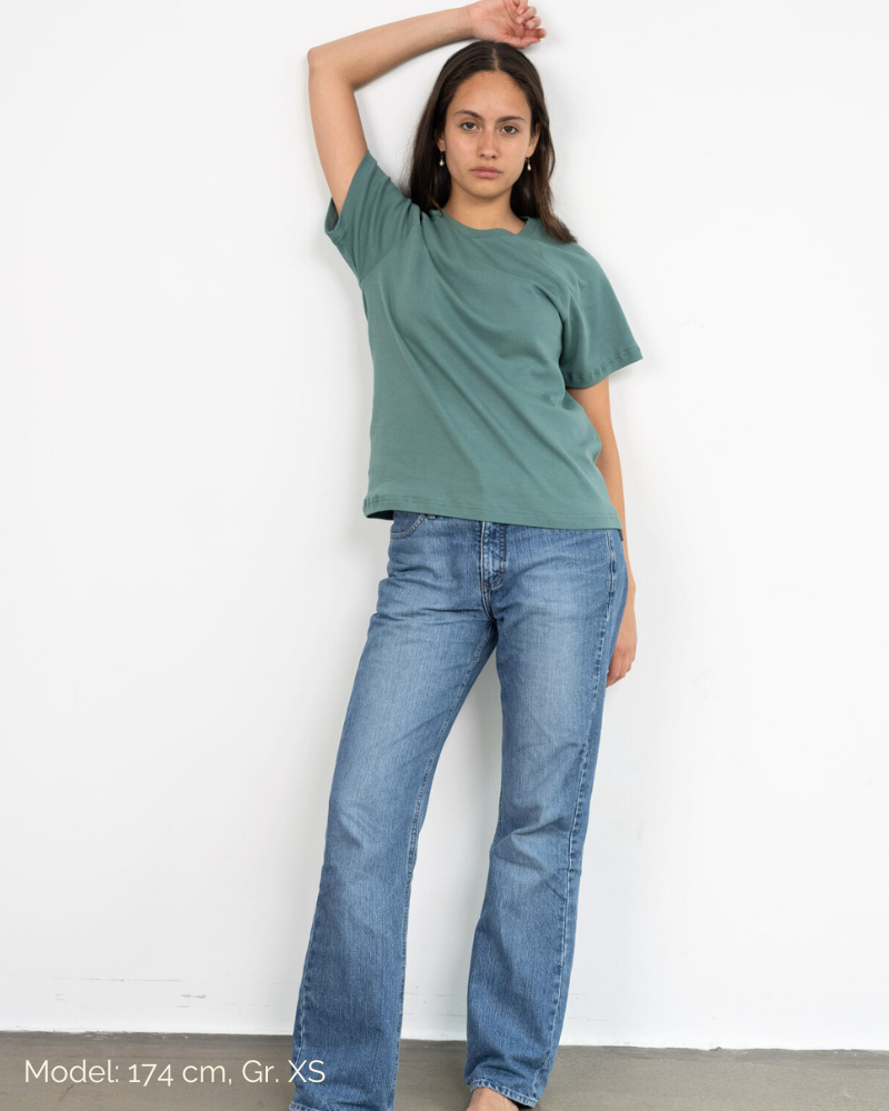 Eine Frau lehnt an einer Wand und trägt ein faires Shirt aus Bio-Baumwolle im Unisex-Schnitt von Oktopulli