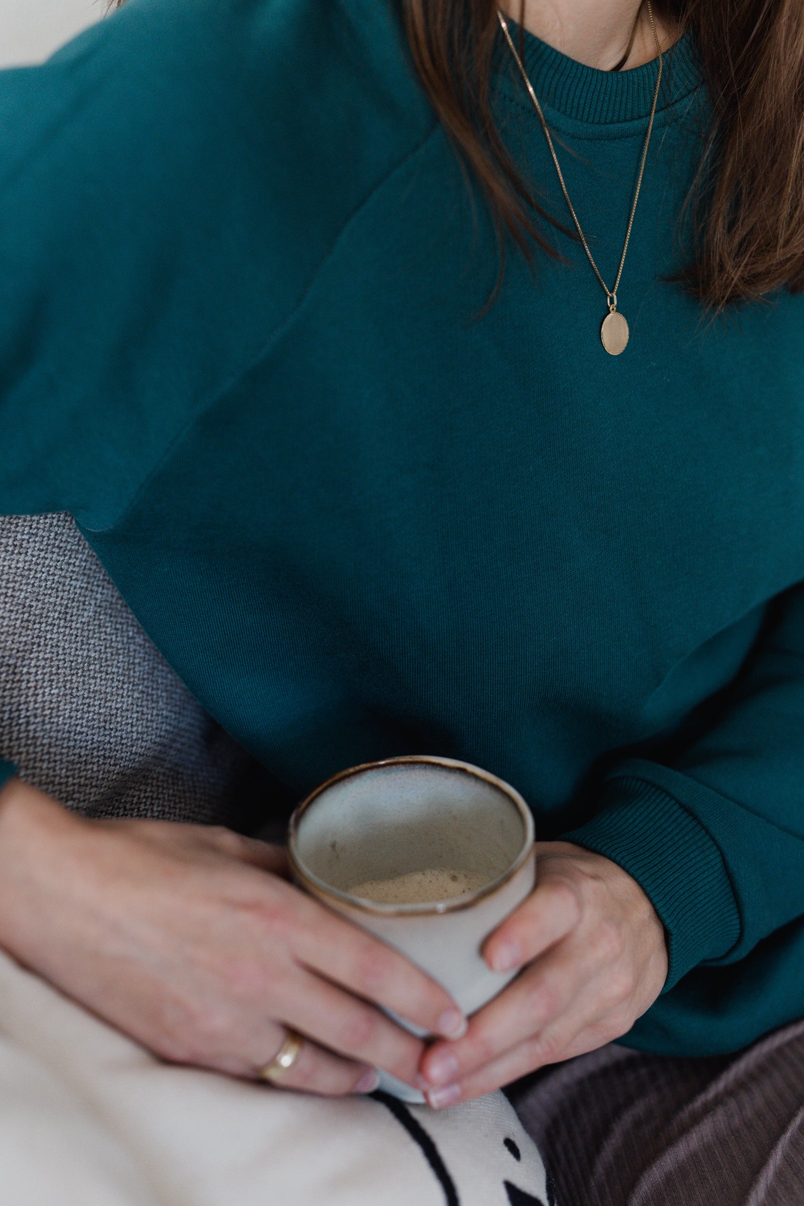 Nahaufnahme von Frau im smaragdgrünen Oktopulli. In ihren Händen hält sie eine Tasse.